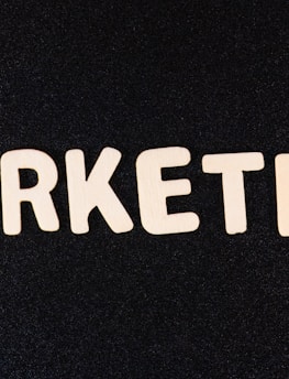 Wooden letters arranged to spell the word 'MARKETING' on a black textured background.