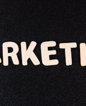 Wooden letters arranged to spell the word 'MARKETING' on a black textured background.